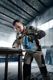 Seseorang yang mengenakan peralatan keselamatan mengoperasikan gergaji ukir untuk memotong lembaran logam.