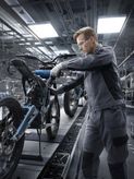 Seseorang yang mengenakan peralatan keselamatan merakit rangka sepeda motor di sebuah pabrik.