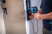 Seseorang menggunakan kamera inspeksi untuk memeriksa pipa di dalam bukaan dinding.