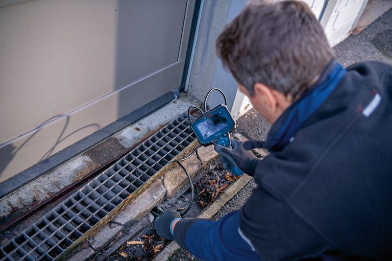 Seseorang yang mengenakan peralatan keselamatan memeriksa saluran pembuangan dengan kamera inspeksi.