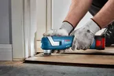 Seseorang yang mengenakan perlengkapan keselamatan menggunakan pemotong multiguna tanpa kabel untuk memotong lantai di dekat pintu.