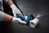 Seseorang yang mengenakan peralatan keselamatan memotong pipa plastik putih dengan pemotong multi-kabel.