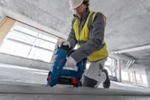 Seseorang yang mengenakan perlengkapan keselamatan menggunakan paku beton tanpa kabel pada lintasan logam.
