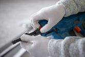 Orang yang mengenakan perlengkapan keselamatan sedang menyetel paku beton tanpa kabel.