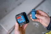 Seseorang memegang alat perataan laser dan baterai.