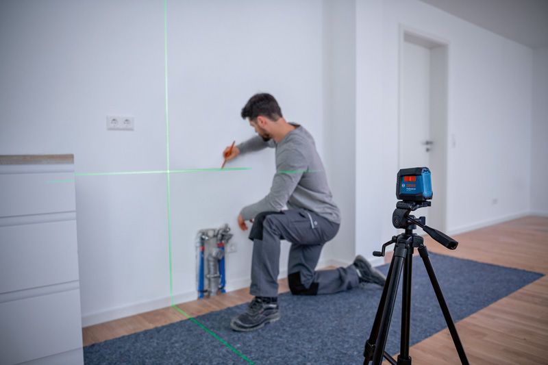 Seseorang menandai dinding menggunakan alat perata laser yang dipasang pada tripod.