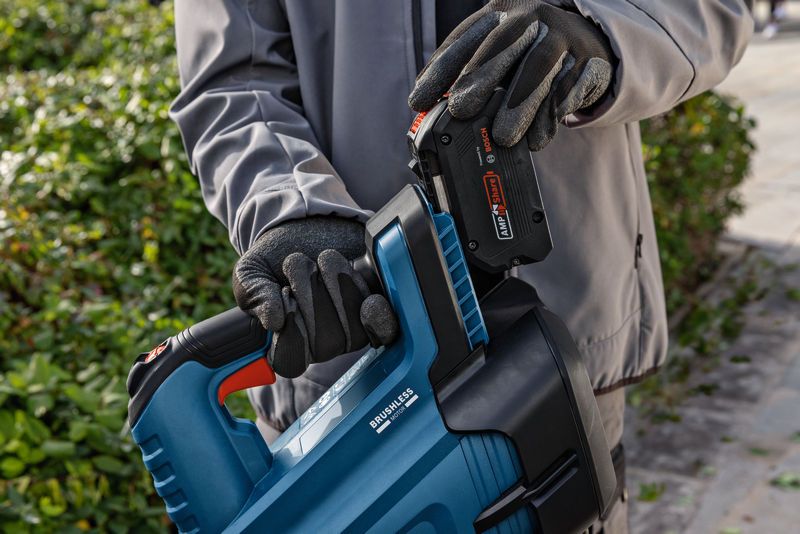 Seseorang yang mengenakan peralatan keselamatan memasukkan baterai ke dalam blower daun nirkabel di luar ruangan.