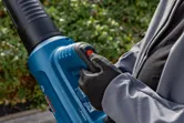 Seseorang yang mengenakan peralatan keselamatan mengoperasikan blower daun tanpa kabel di luar ruangan.