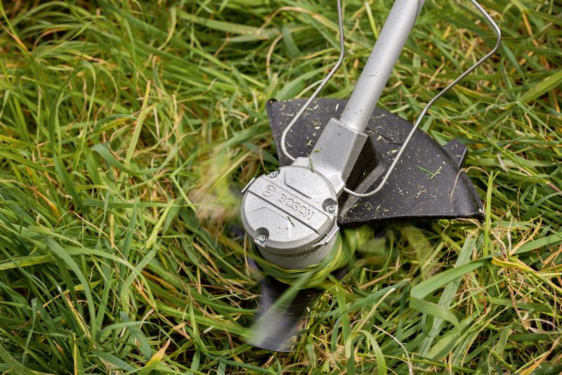 Pemotong sikat tanpa kabel memangkas rumput tinggi dengan bilah yang berputar.