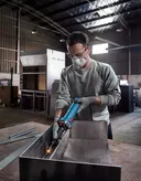 Seseorang yang mengenakan peralatan keselamatan menggiling logam di dalam bengkel industri.