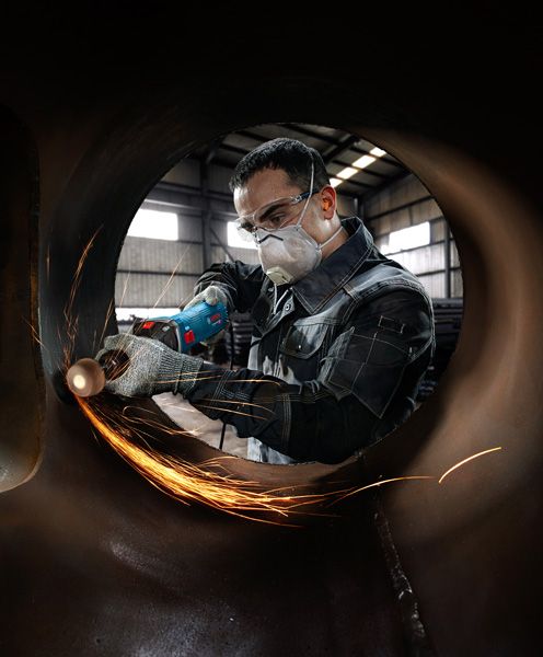 Seseorang yang mengenakan peralatan keselamatan menggiling logam di dalam pipa besar, sehingga menimbulkan percikan api.