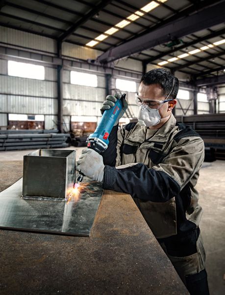 Seseorang yang mengenakan perlengkapan keselamatan menggunakan penggiling lurus pada lembaran logam.