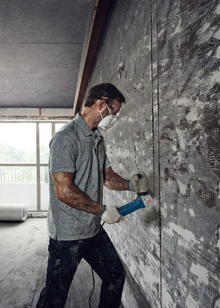 Seseorang yang mengenakan perlengkapan keselamatan menggunakan penggiling sudut untuk memotong dinding beton.