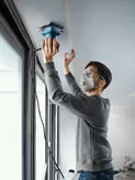 Seseorang yang mengenakan peralatan keselamatan mengampelas tepi langit-langit dengan sander orbital.