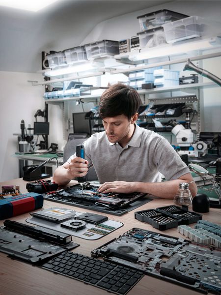 Orang yang merakit perangkat elektronik dengan obeng tanpa kabel di bengkel.