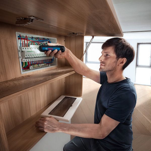 Seseorang mengamankan kabel di panel listrik menggunakan obeng tanpa kabel.