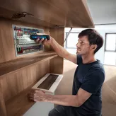 Seseorang mengamankan kabel di panel listrik menggunakan obeng tanpa kabel.