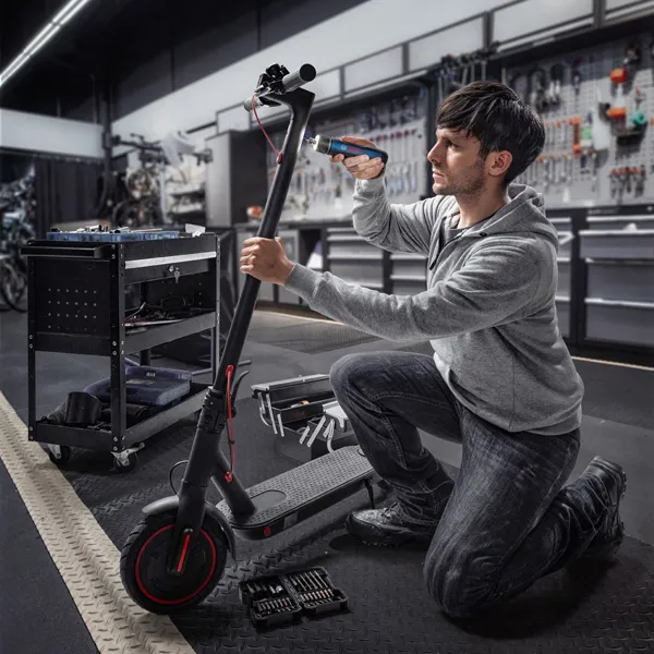 Seseorang berlutut dan menggunakan obeng tanpa kabel untuk memperbaiki skuter listrik.