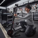 Seseorang berlutut dan menggunakan obeng tanpa kabel untuk memperbaiki skuter listrik.