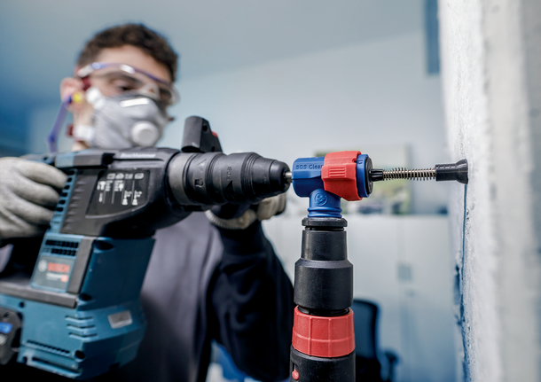 Orang yang mengenakan peralatan keselamatan mengebor dinding menggunakan bor palu.