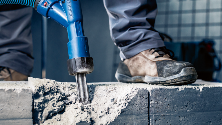 Orang yang mengenakan peralatan keselamatan memecahkan beton dengan alat listrik.