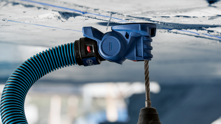 Alat penyedot debu yang dihubungkan ke bor membuat lubang di langit-langit beton.