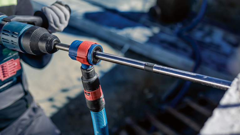 Seseorang yang mengenakan perlengkapan keselamatan menggunakan alat putar untuk mengebor beton.