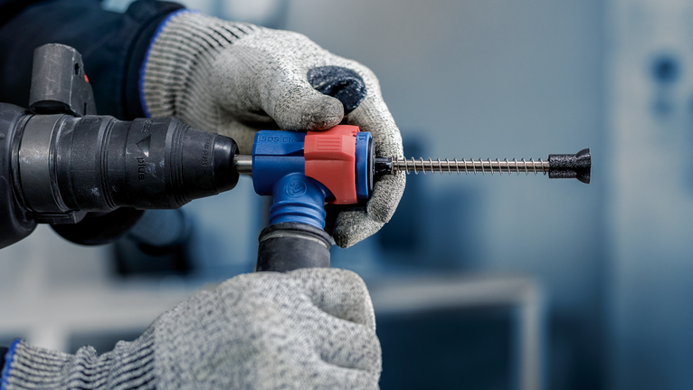 Tangan bersarung tangan memegang bor palu putar dengan mata pahat, mengenakan peralatan keselamatan.