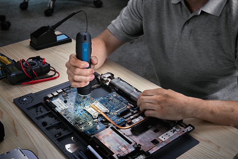 Seseorang menggunakan obeng tanpa kabel untuk merakit laptop di meja kerja.