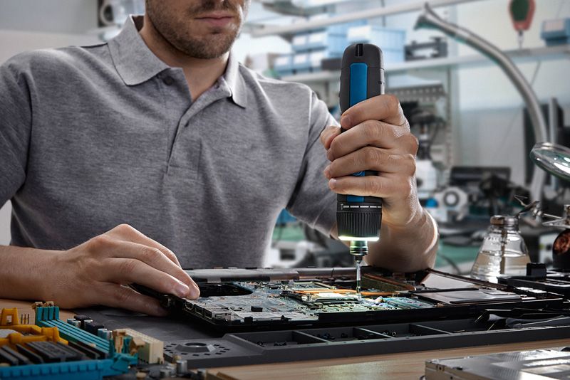 Orang yang menggunakan obeng tanpa kabel untuk merakit komponen elektronik pada papan sirkuit.