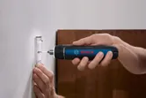 Seseorang menggunakan obeng tanpa kabel untuk mengencangkan sekrup ke pelat sakelar dinding.