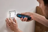Seseorang menggunakan obeng tanpa kabel untuk mengencangkan sekrup pada panel sakelar lampu.