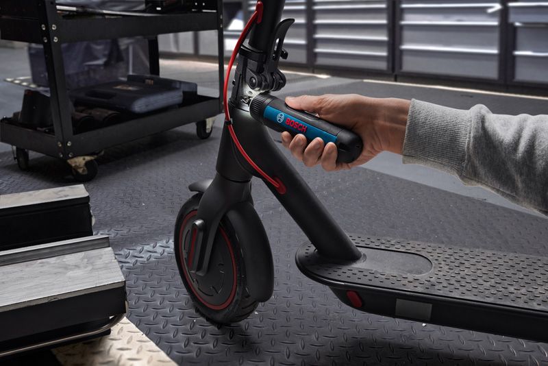 Seseorang menggunakan obeng tanpa kabel untuk menyetel stang skuter listrik.