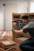 Orang yang mengenakan peralatan keselamatan memasang slide laci lemari menggunakan bor tanpa kabel.