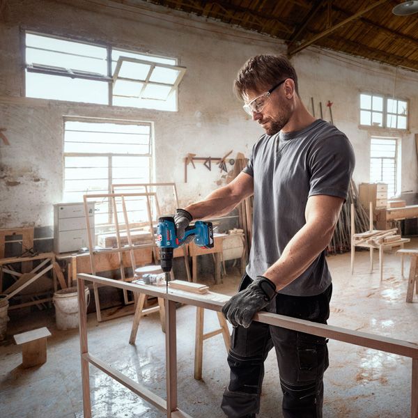 Seseorang yang mengenakan perlengkapan keselamatan mengebor rangka kayu di bengkel.