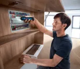 Seseorang menggunakan obeng tanpa kabel untuk mengencangkan komponen pada panel listrik.