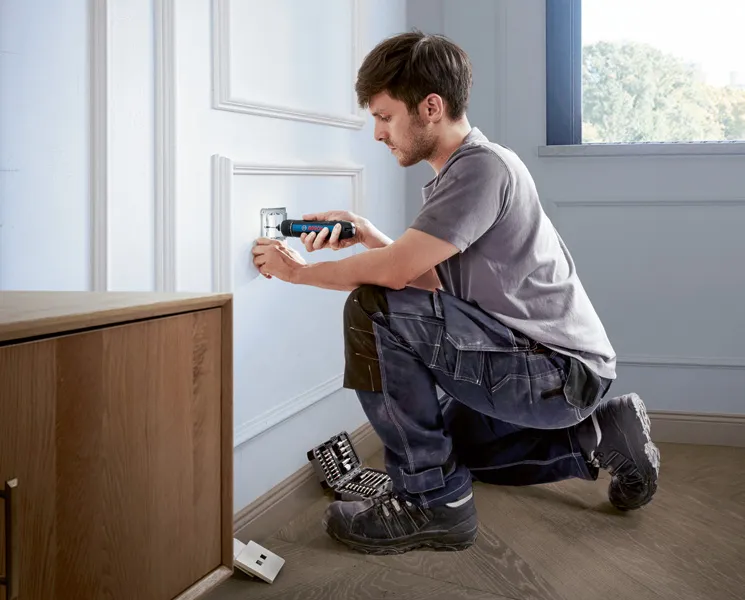 Seseorang menggunakan obeng tanpa kabel untuk memasang penutup stopkontak listrik.