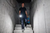 Seseorang memegang lampu kerja nirkabel dan kotak peralatan sambil menuruni tangga beton.