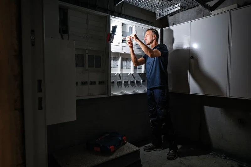 Seseorang bekerja pada panel listrik yang diterangi oleh lampu kerja nirkabel.