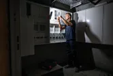 Seseorang bekerja pada panel listrik yang diterangi oleh lampu kerja nirkabel.