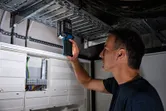 Orang yang memeriksa panel listrik menggunakan lampu nirkabel di ruang utilitas.