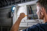 Seseorang menggunakan obeng pada panel listrik, lampu nirkabel terpasang untuk penerangan.