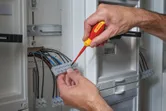 Seseorang menggunakan obeng berisolasi untuk mengencangkan kabel di panel listrik.