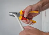 Seseorang menggunakan tang berisolasi untuk mencengkeram dan membengkokkan kabel putih tebal.