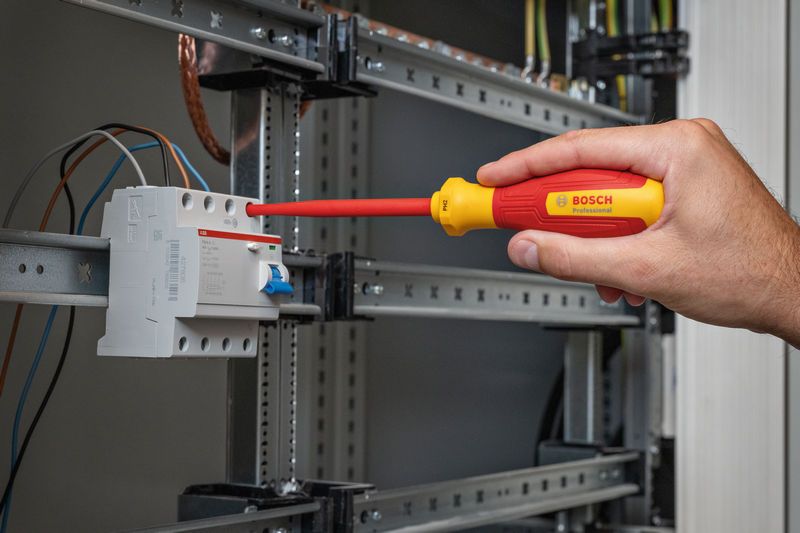 Seseorang mengencangkan sekrup terminal pada panel listrik dengan obeng berisolasi.