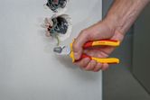 Seseorang menggunakan tang berisolasi untuk memotong kabel hijau dari kotak dinding listrik.