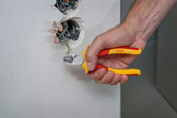 Tang Potong Diagonal VDE 160 mm Seseorang menggunakan tang berisolasi untuk memotong kabel hijau dari kotak dinding listrik.