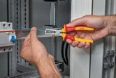 Seseorang melepaskan isolasi dari kabel biru di lemari listrik.