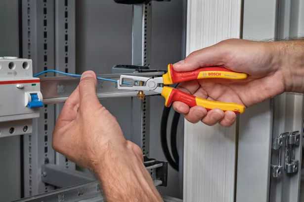 Pengupas kabel universal VDE 160 mm Seseorang melepaskan isolasi dari kabel biru di lemari listrik.