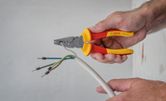 Orang melepaskan isolasi dari kabel listrik menggunakan tang berisolasi.